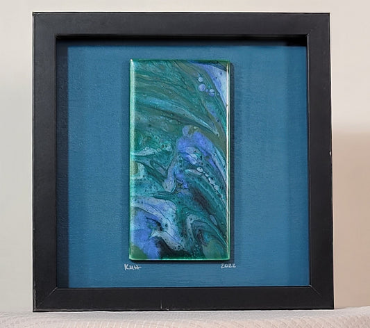 Shadow box with a black frame and a teal blue background with a tile mounted on it; just under the tile, the artist has signed their initials KMH and the date 2022. The tile have bands of darker and lighter green mixed with sapphire blue and light blue. There are bubbles of color within the bands.