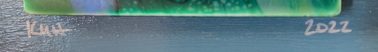 A close-up detail of the base of the tile (largely out of focus green bands and bubbles) to highlight the authors initials KMH and year completed 2022.