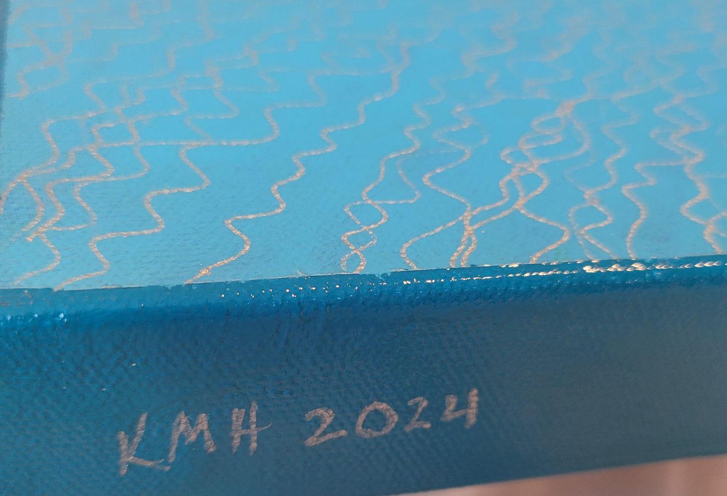 A view of the blue side edge of the painting with the artist's initials "KMH" and year completed "2024." The light blue and silver squiggly lines of one portion of the painting are visible.