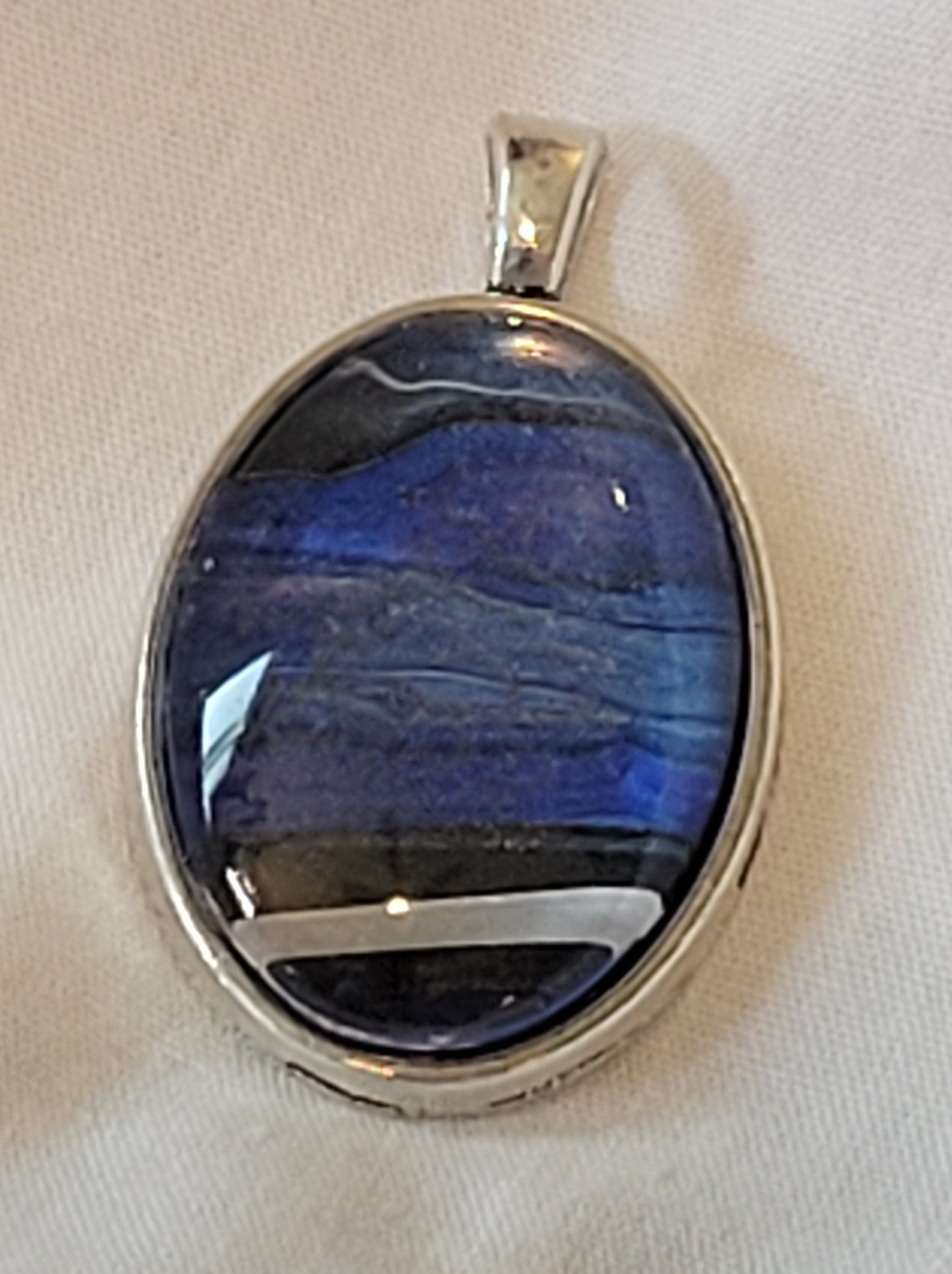 A close-up detail of the pendant, highlighting the fuzzy, nebula "cloud" structure of the blues with the stark and harsh black and white/silver banding at the bottom of a black hole event horizon. The pendant is a simple silver outline with no additional adornment.