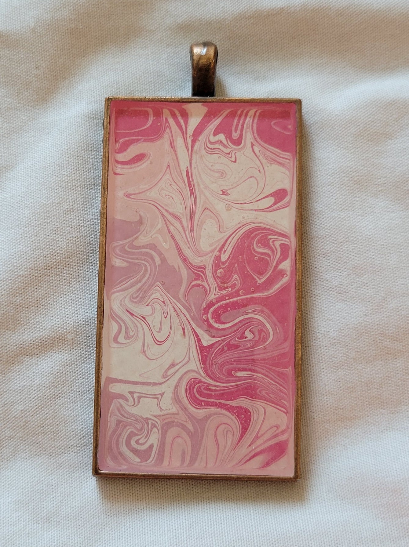 A close-up of the pendant with the bronze setting. The swirls of pinks, lavender, and white are more clear, showing swirls within swirls and numerous color encroachments.