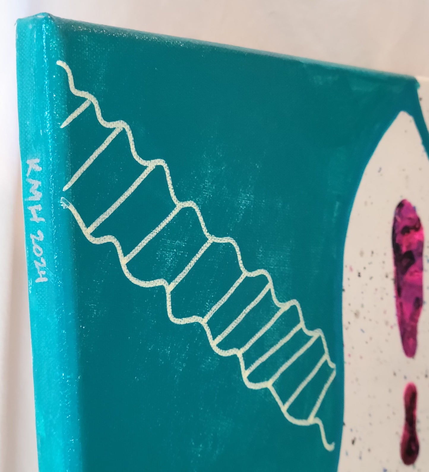 Close-up detail of a corner of the canvas featuring the artist's initials "KMH" and year completed "2024" written in silver on the edge. The front of the canvas that can be seen is a large section painted teal with an off-white double-helical pattern.