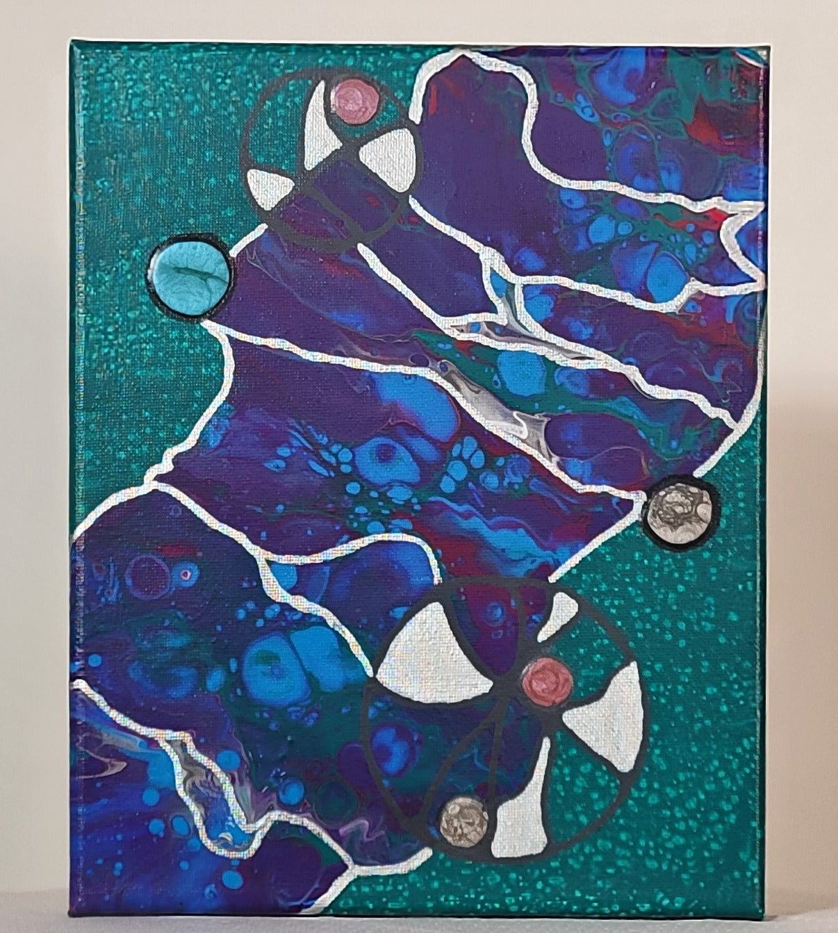 Against a distressed forest green background, a large spill of fluid acrylic in purple, blue, green, and magenta stretches the diagonal of the canvas. The stretch of fluid acrylic is outlined in silver. Transparent circles in gray bud out from the spill of fluid acrylic and have sections painted silver and vesicles of alkyd oil. Silver threads through the fluid acrylic spill in a fibrous pattern.