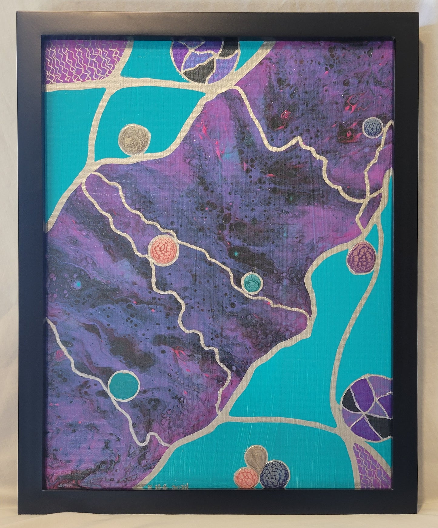 A black-framed canvas panel painted turquoise with a diagonal pour of fluid acrylic in purple, pink, and blue-black colors. Silver outlines the pour as well as lines intersect outside of and thread through the pour. The intersecting areas a the opposite corners of the panel are painted a pink-blue with silver squiggly lines. Alkyd oil cirlces and purple-black multi-colored balls flow along the silver lines.