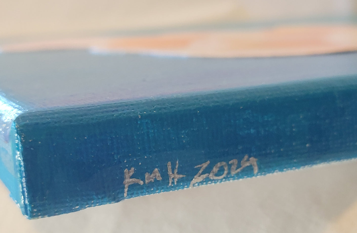 Close-up of the blue edge of the canvas with the artist's initials "KMH" and year completed "2024" written in silver.