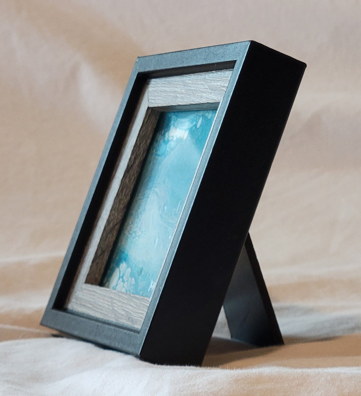 A mostly side-on view of the frame, demonstrating the stand it can use to rest on a desk surface. The art is largely obscured, but some of the white bubbles and waves are visible in the mostly blue square.