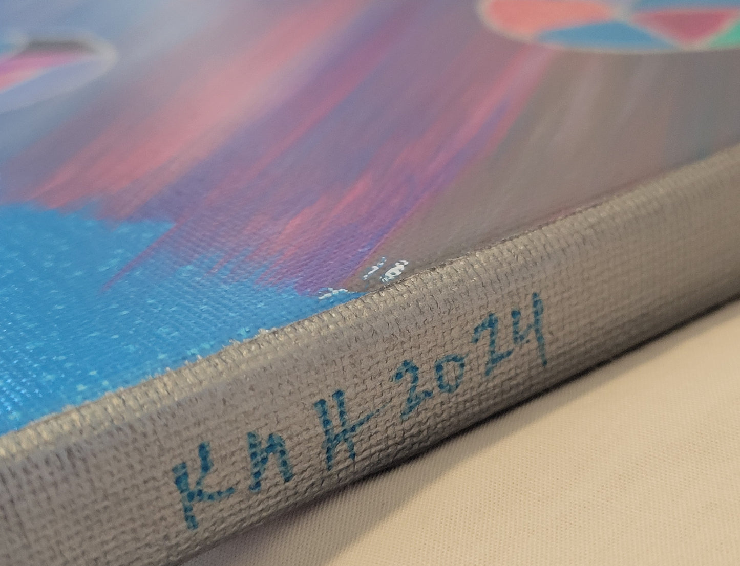 The silver edge of the canvas is shown with the artist's initials "KMH" and year completed "2024" written in blue.