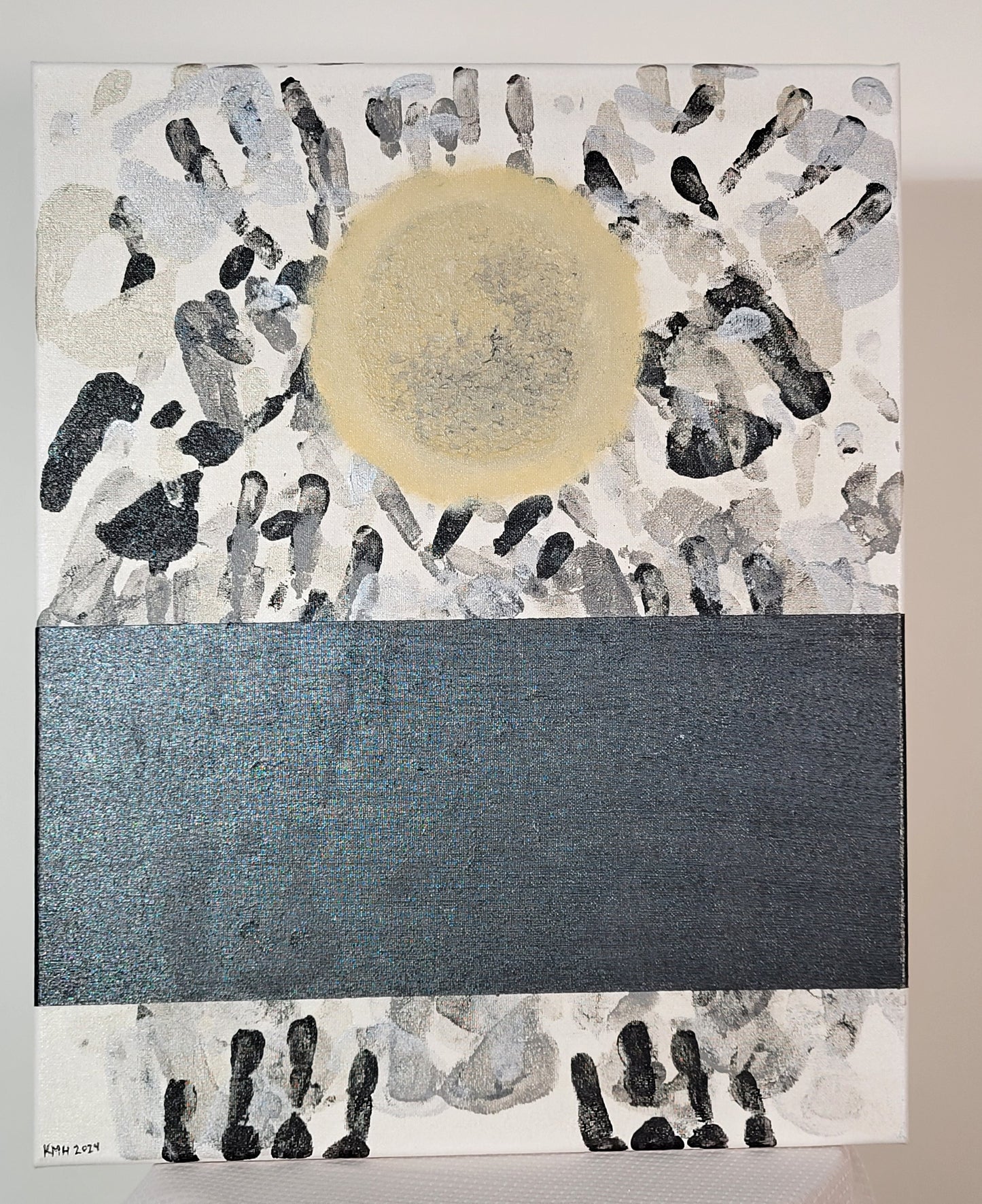 A slightly stained white canvas is littered with handprints in black, gray, silver, and pewter. A yellow full moon oversees the piece, glowing ominously, showing it's gray-pocked surface. A space-black band covers a portion of the bottom of the canvas. If you look just right, you can see the glossy outline of a single set of handprints in that band. Acrylic and gloss gel on canvas.