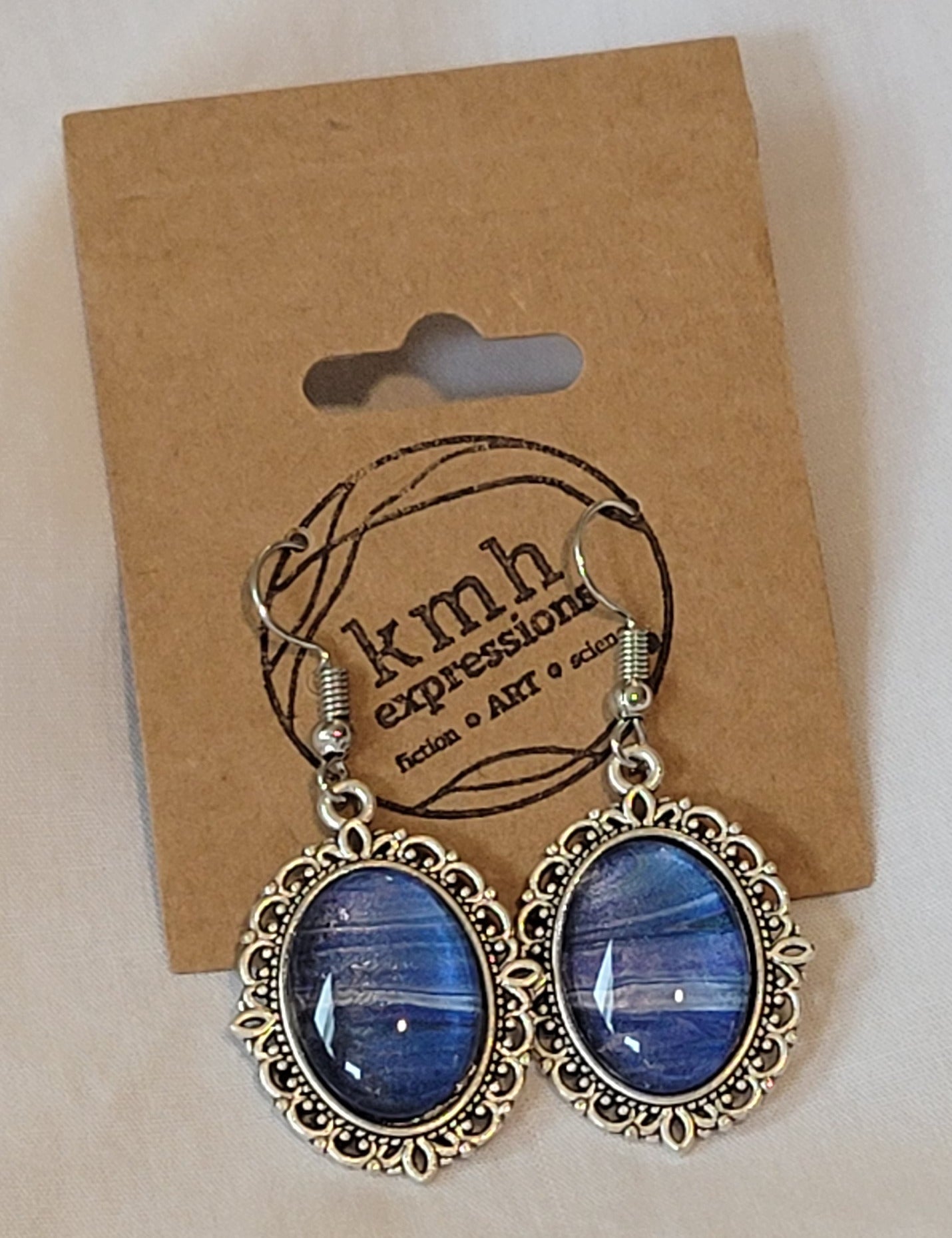 Decorative filigree borders the simple silver settings of these earrings. The distinctions between the purple, silver, and blue is a bit more stark, but the patterns of banding flow easily from one earring to the other, as if the wind carries directly through them.