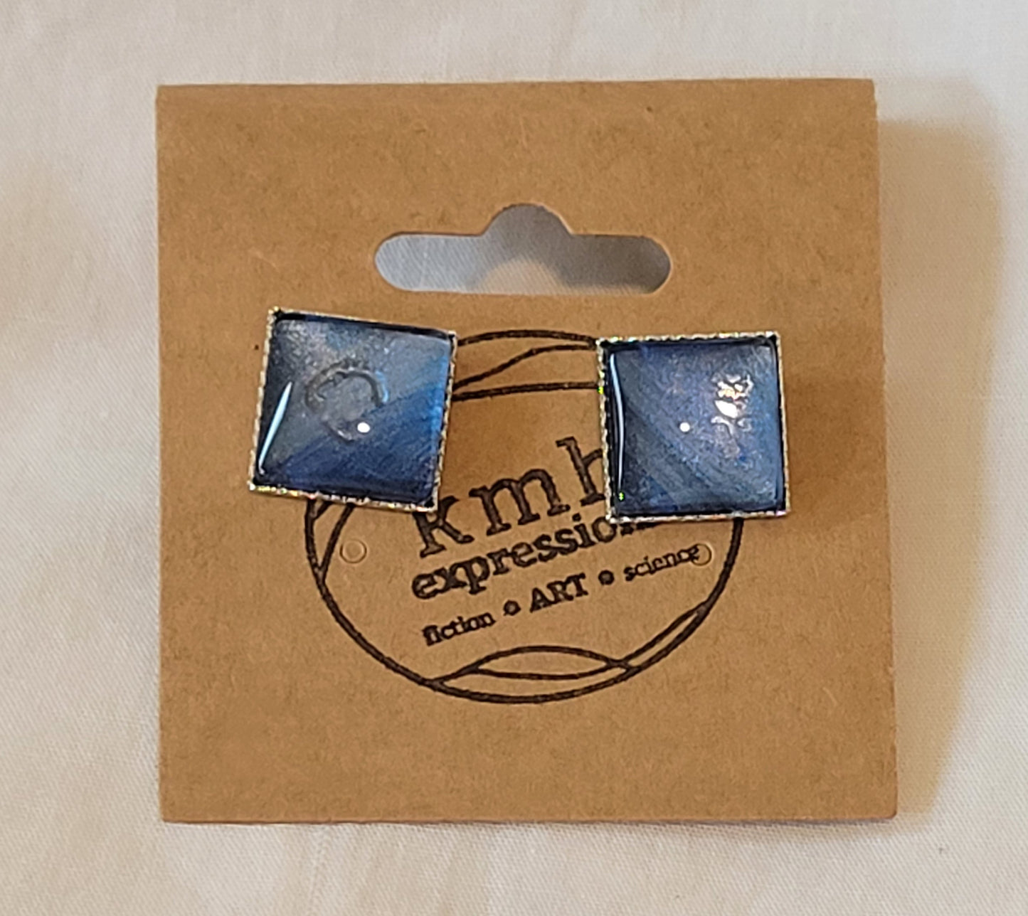 Square stud earrings on a brown card stamped with the kmh expressions logo. The earrings are subtle in their blue, purple, and silver gradients and banding.