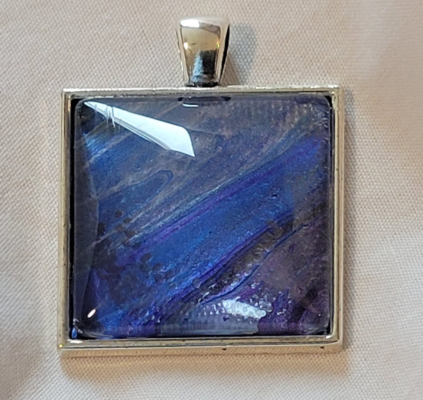 A simple silver setting for the cabochon featuring deep blues and purple banding with wisps of silver.