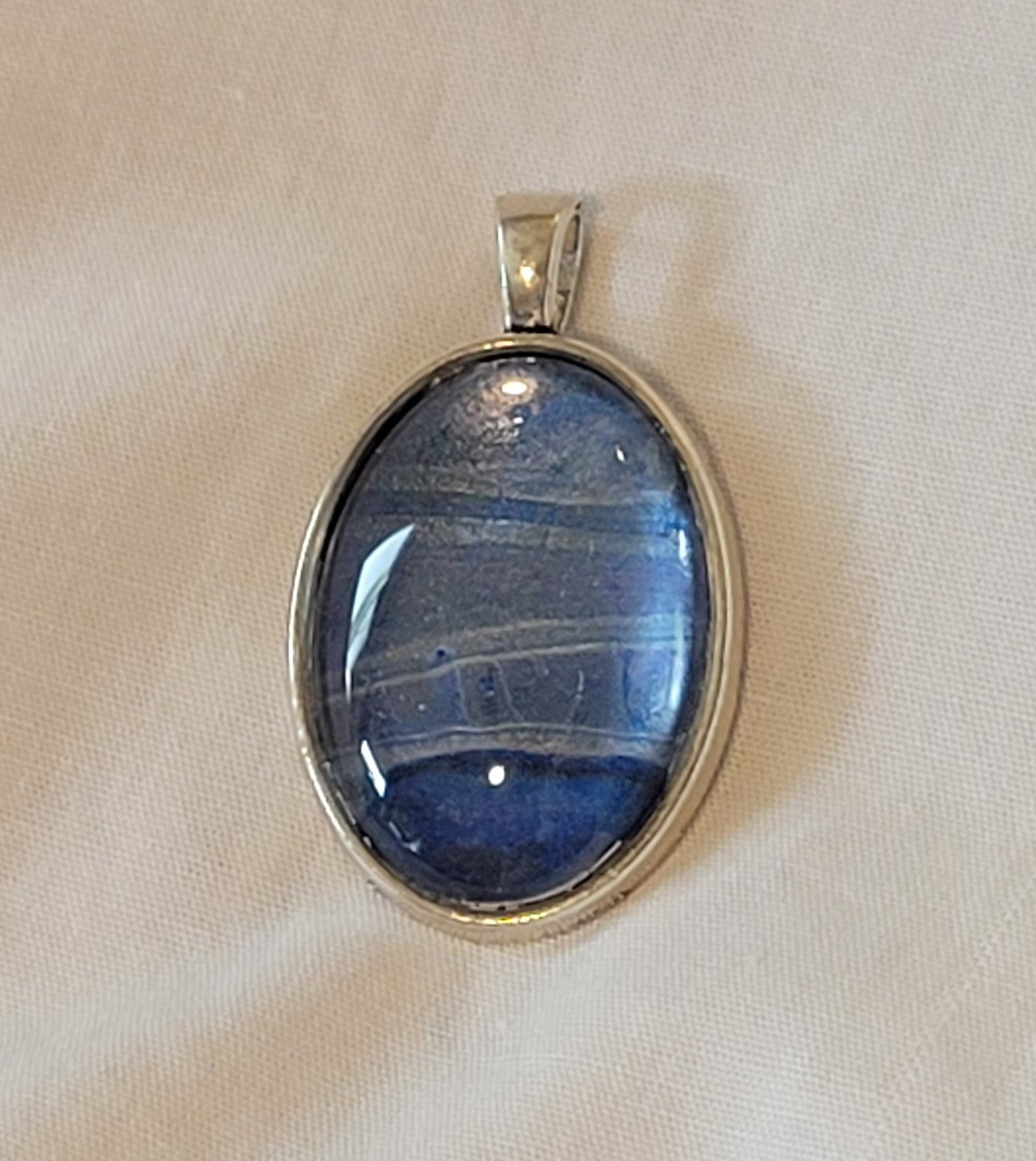 Simple silver setting highlights the subtle banding between purple, silver, and blue across the cabochon.