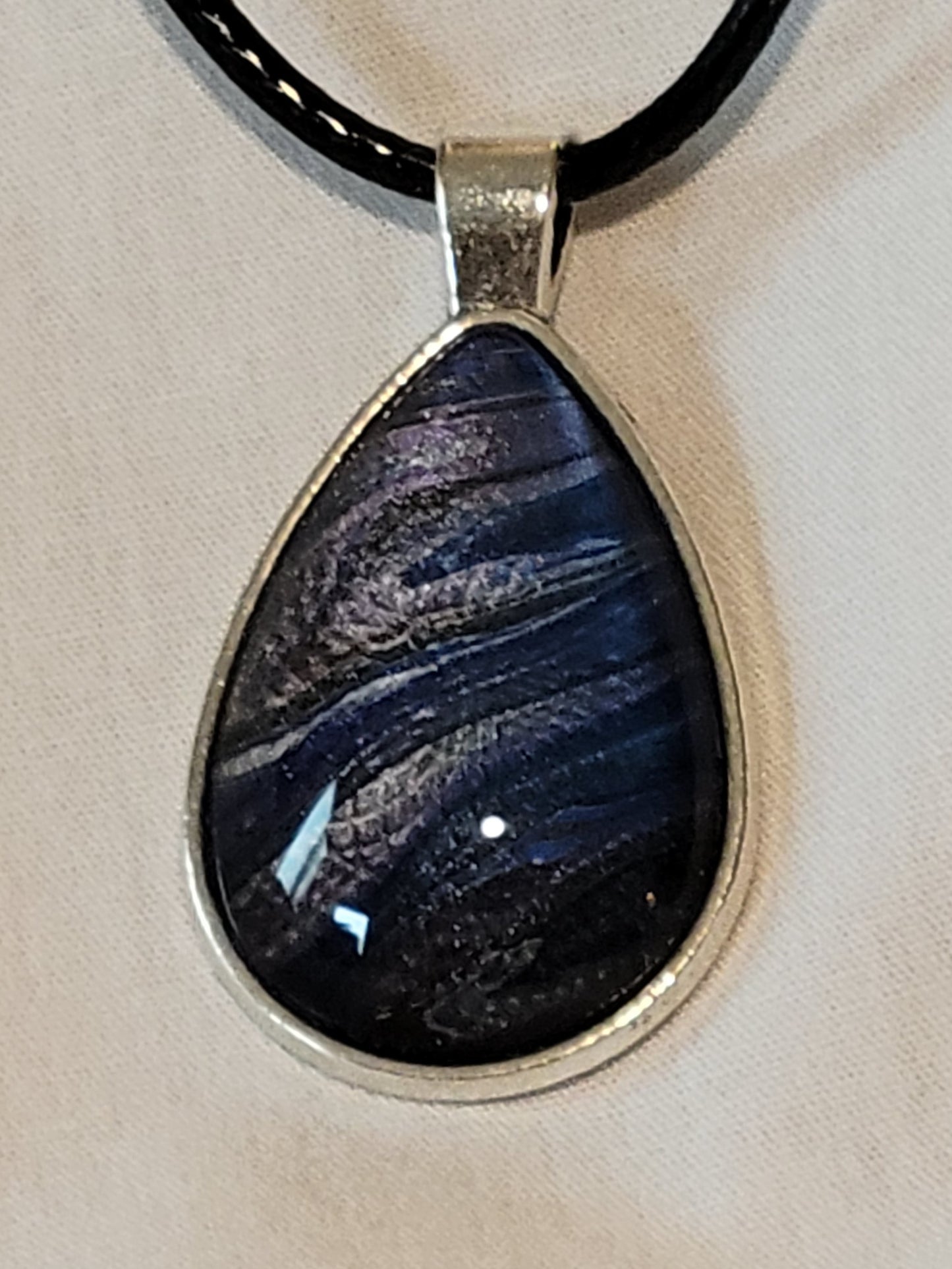 Simple silver setting for a cabochon with dark blue, purple, and black coloring, threaded through with silver in streaks that resemble air currents.