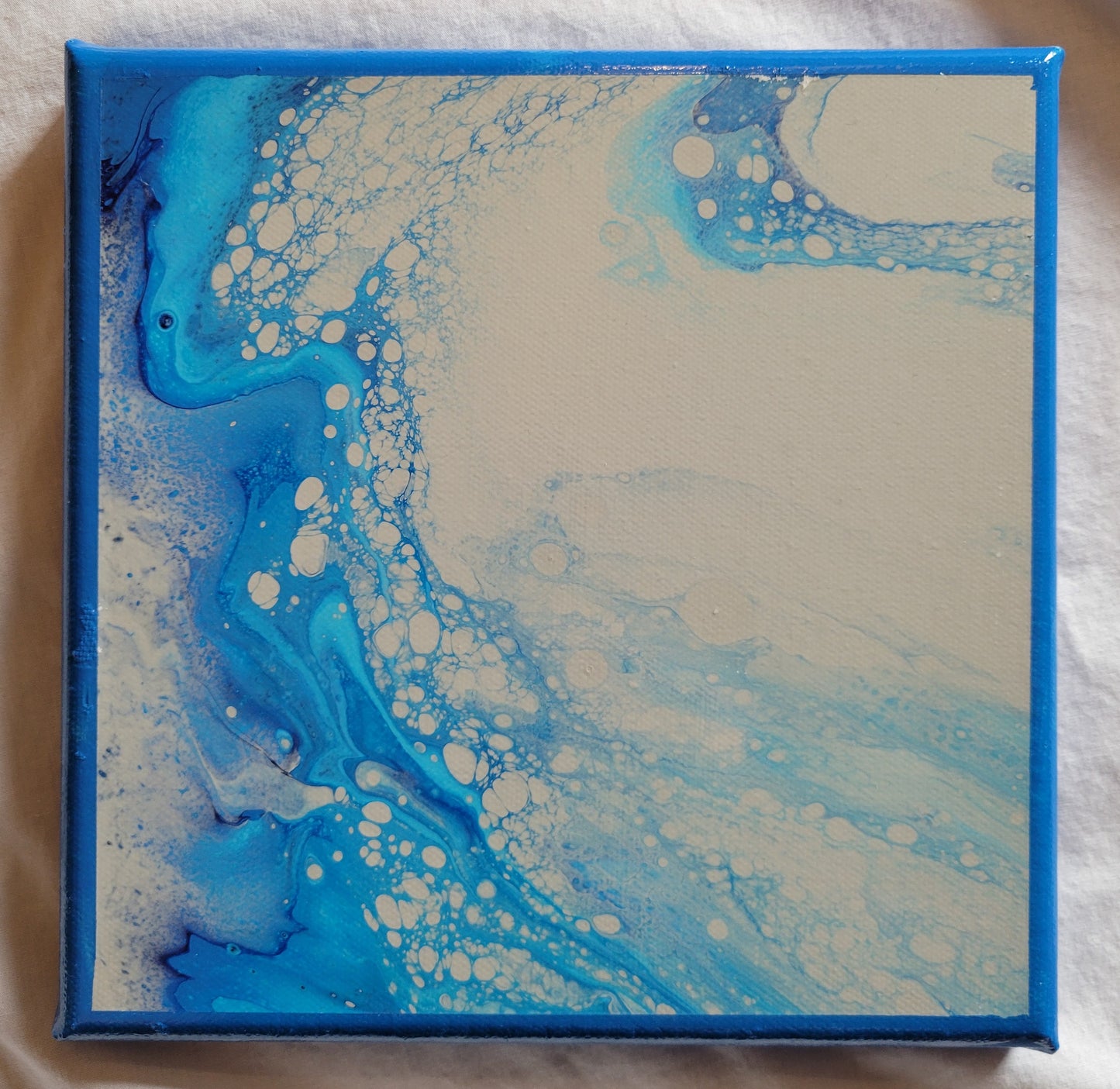 An 8x8 canvas featuring a bright turquoise blue and darker sky blue swirling and bubbling around a light sandy brown. The flow is such that it looks like waves crashing in a very sandy churn.