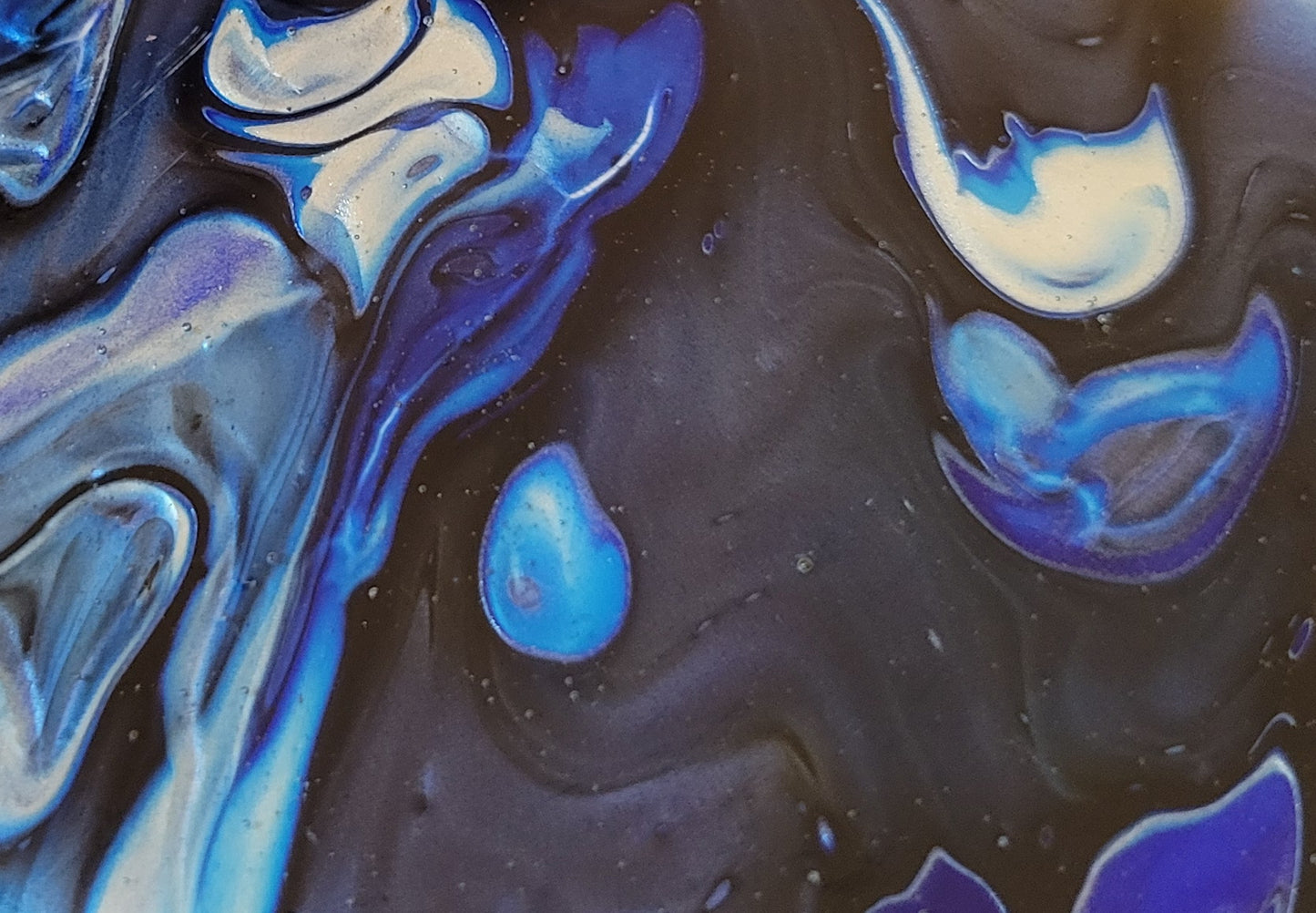 Close-up detail of the color blots on the black background, showing the layers of silver, light blue, and dark blue on each other.