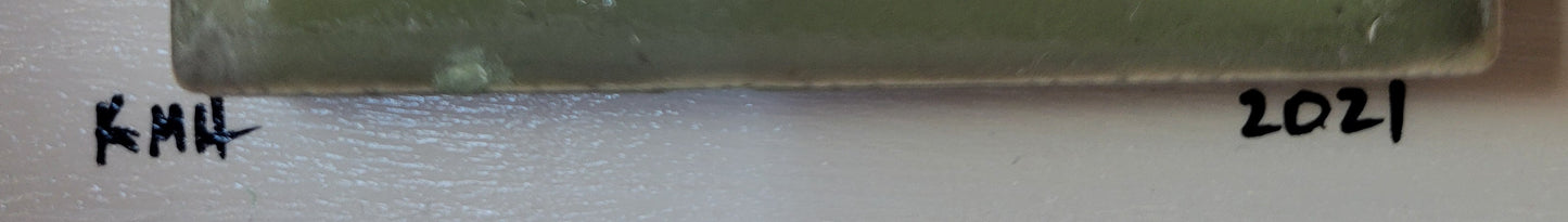 Close-up of the base of the tile where it is affixed to the off-white board, highlighting the artist's initials "KMH" and year completed "2021" in black.