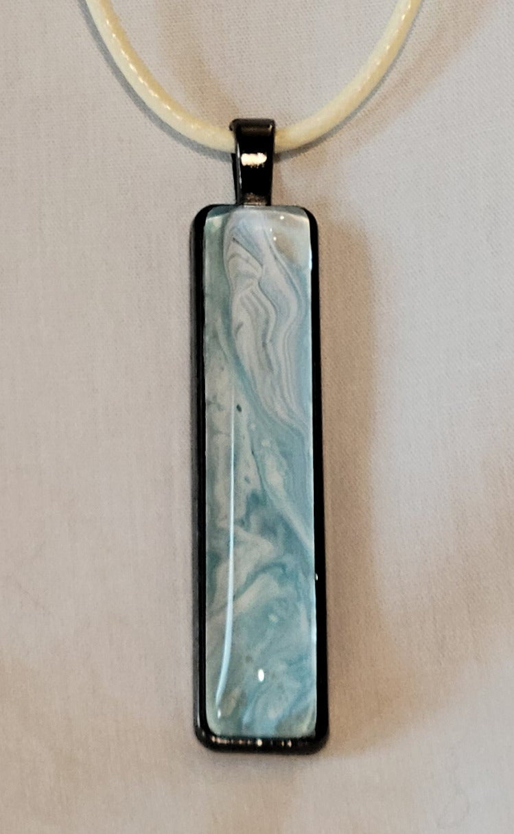 A simple black stainless steel rectangular pendant with a cream-colored imitation leather cord. The pendant has swirls of teal and white layered and swirling on each other like a calming ocean surf.