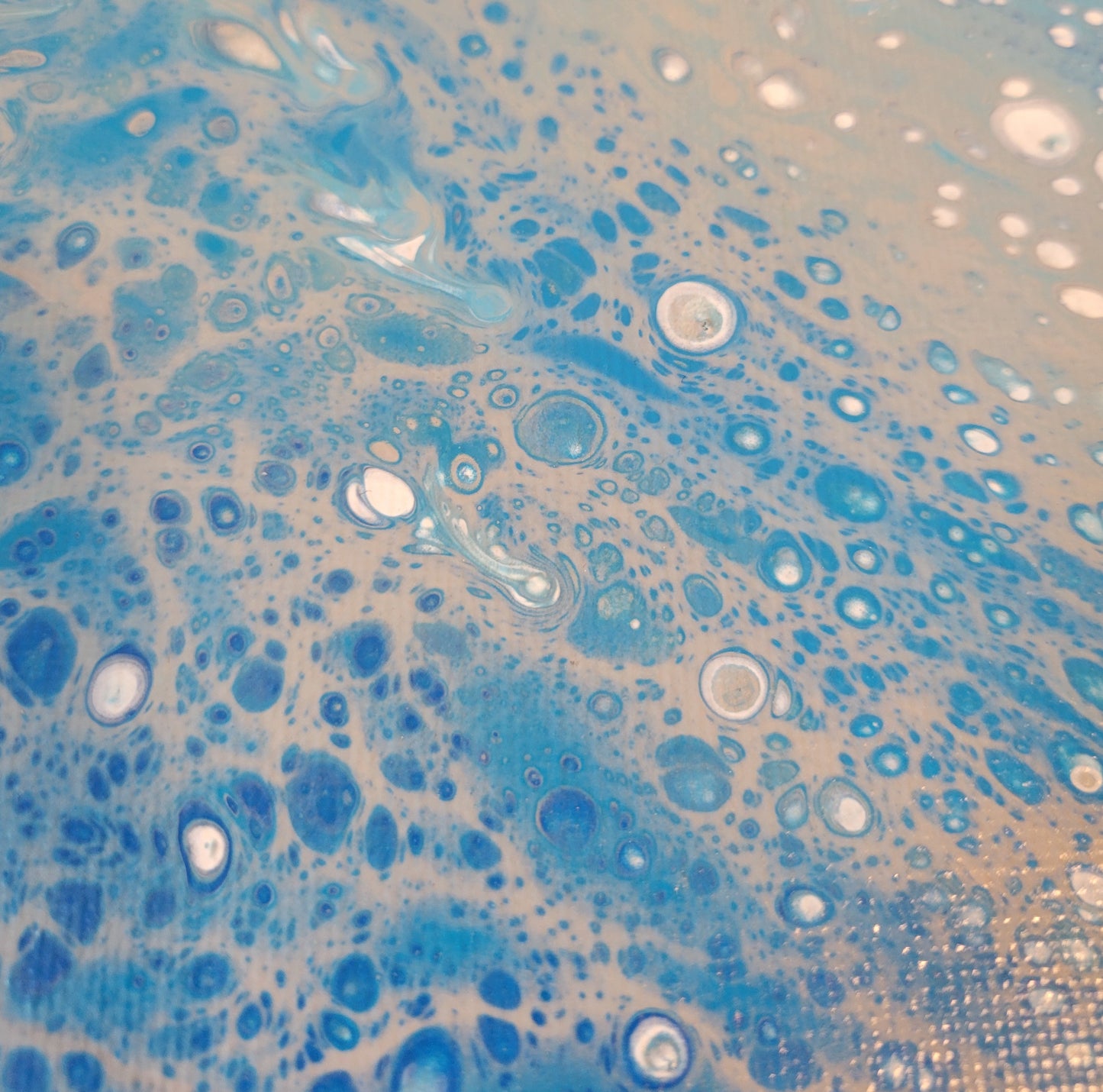 Close up detail of the wave that shows the bubbles of white, blue, and dark blue peeking up through a sandy brown.