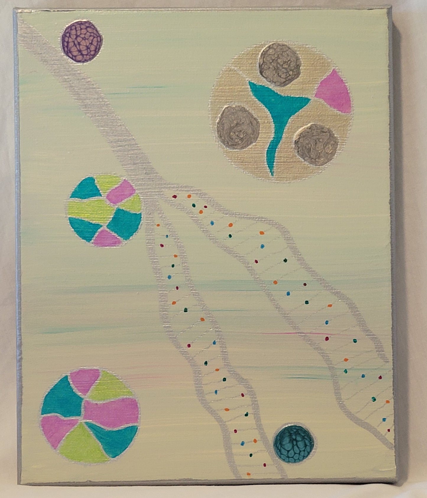 Canvas painted with a background of beige threaded through with blue and pink. Silver stylized unraveling strands of DNA stretch across the diagonal of the canvas. In the unraveled portion, silver lines connect colorful dots along the threads. Multi-colored balls with blue, green, pink, silver and alkyd oil float against and near the unraveling DNA.
