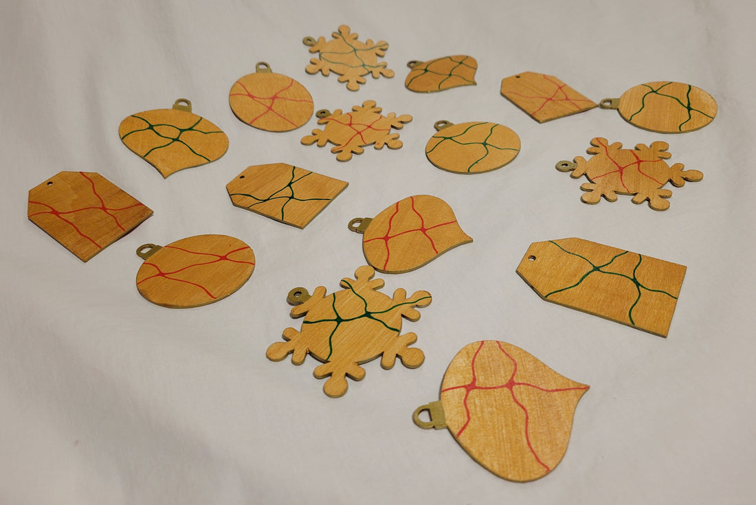 Several wood-cut holiday ornaments shaped as a gift tag, ball, snowflake, and oblong onion are painted gold and decorated with red or green lines.