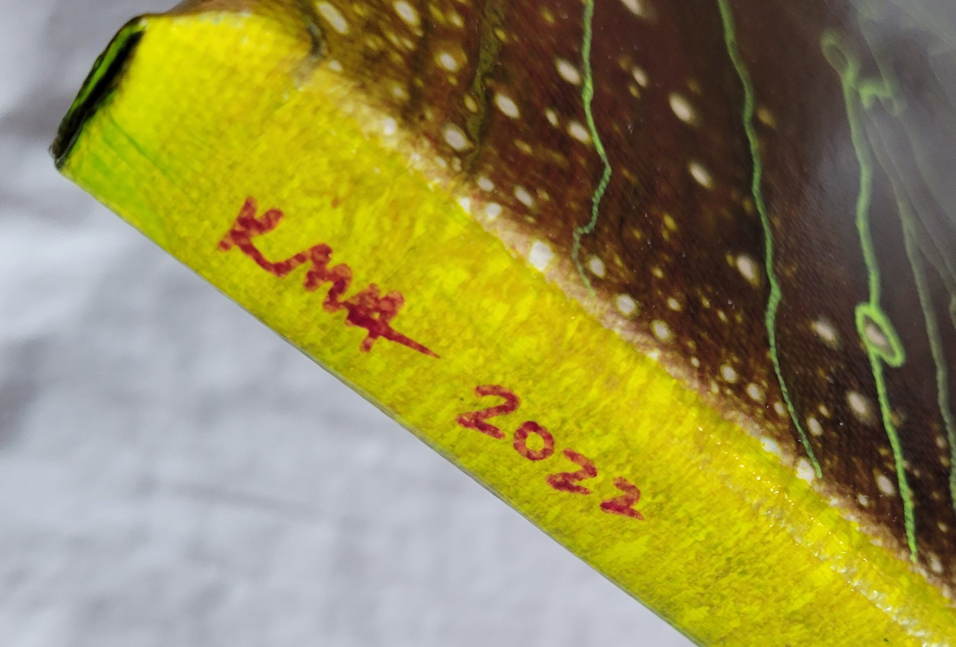 Closeup detail of the authors initials and date of completion "KMH 2022" in bright purple against a vibrant olive green.
