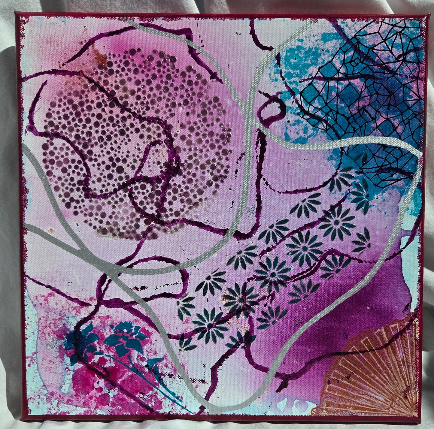Acrylic inks in purple and teal are spilled and stamped haphazardly across the canvas. Stencils of a moon and daisy chains are filled in with purple and teal gloss gel. Stencils of fans, flowers and geometric designs are finely lined in in other corners. Silver and violet lines float over and under it all.