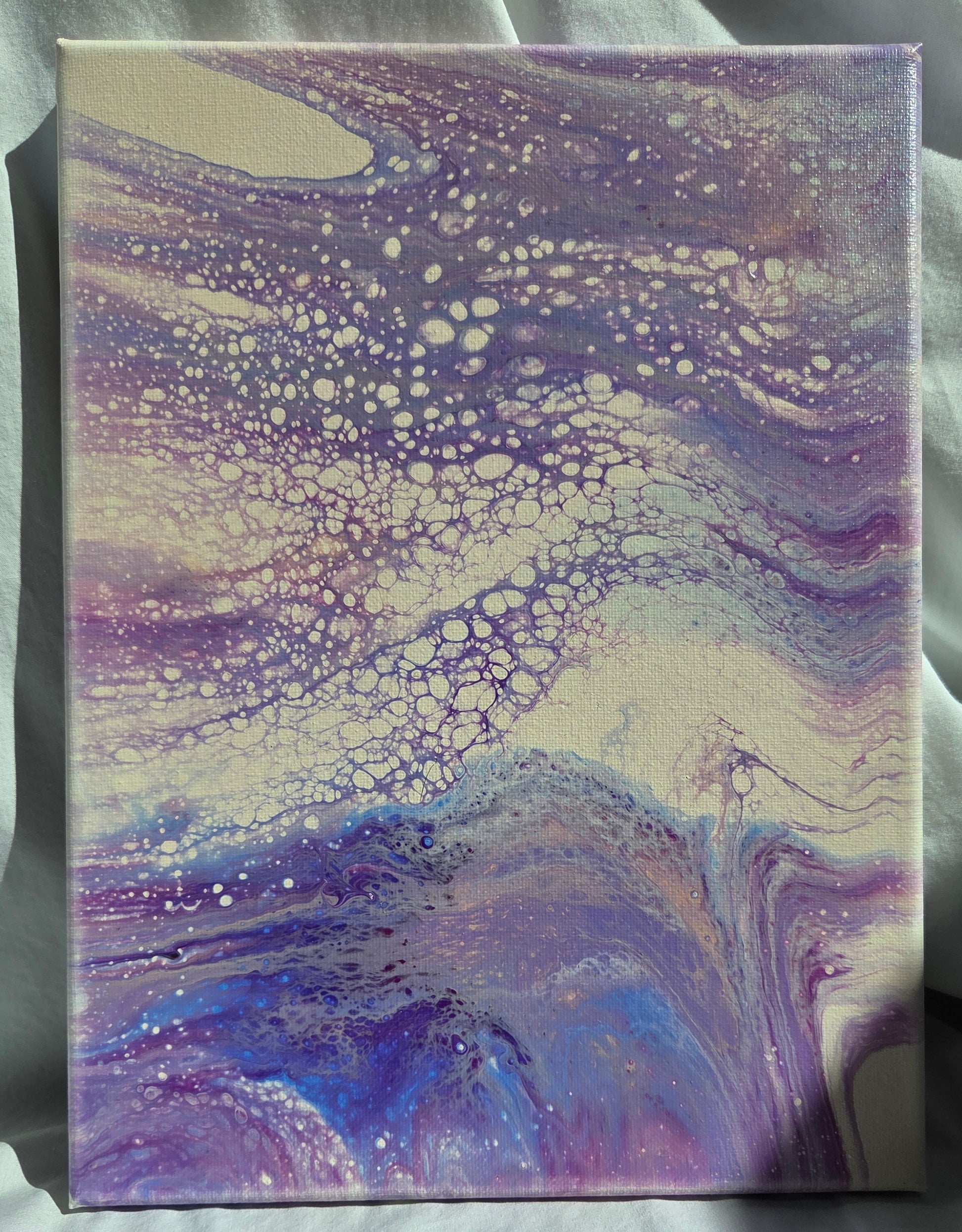 Fluid art piece with purples, blues, and pinks spill and tumble and froth over each other against a beige background.