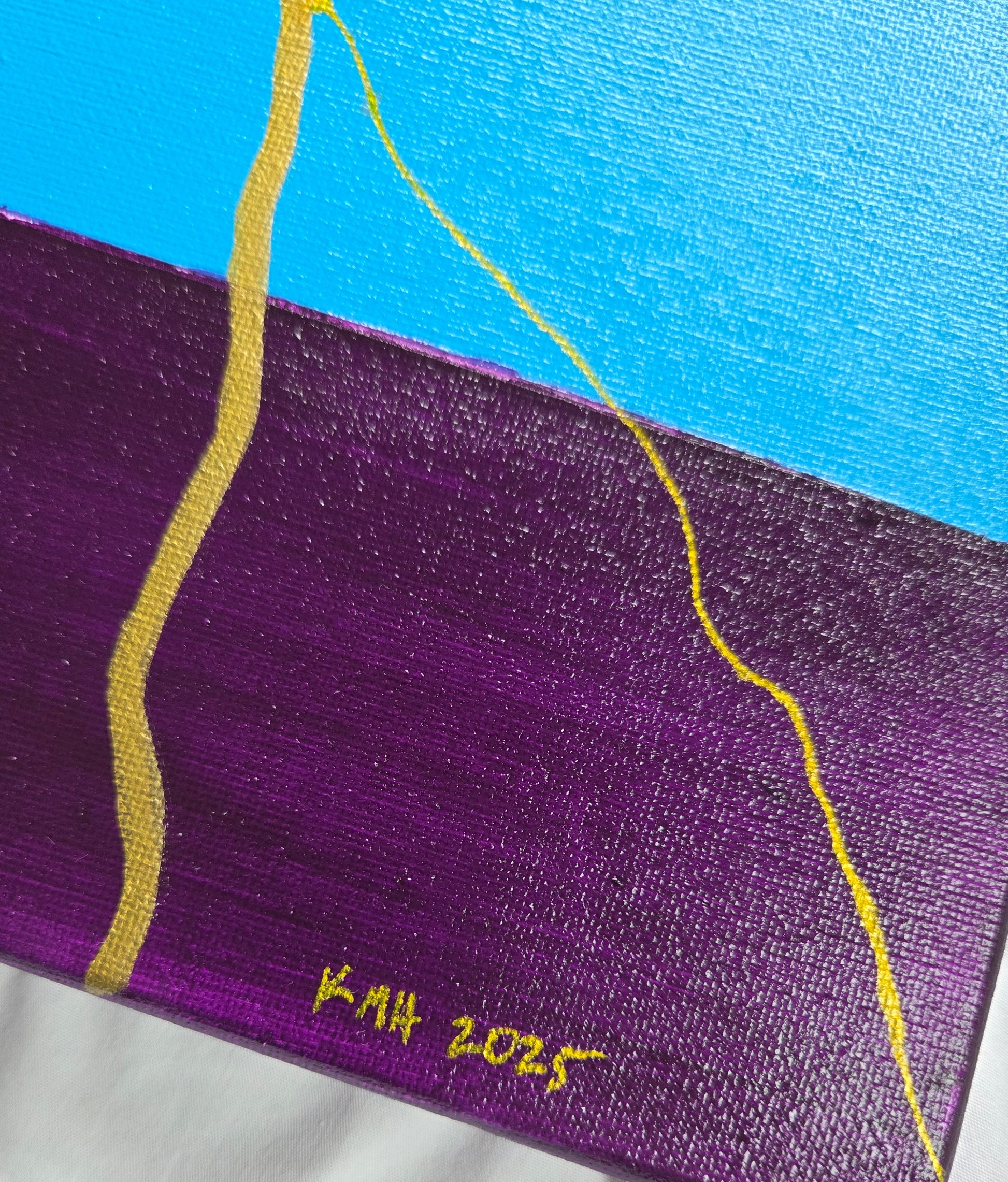 Detail of the blue and violet bands of the pride flag with thin and thick gold lines as well as the artist's initials and year of creation.