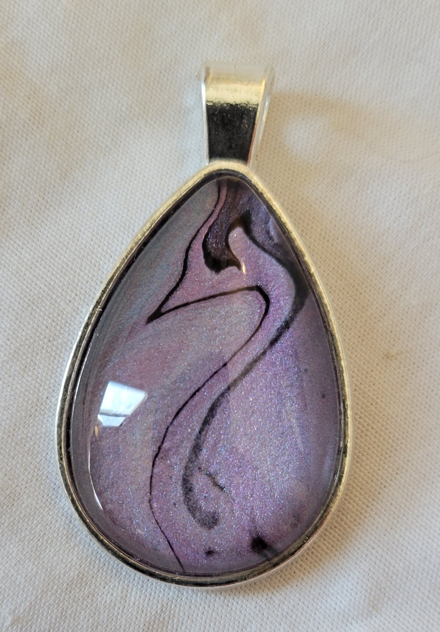 Simple stainless steel teardrop setting with a largely purple and pink cabochon that sparkles, though there are hints of blue at the edges. There is a threading of black through the colors that calls to mind the elegant curve of a swans neck leading to a head with a beak and plume.