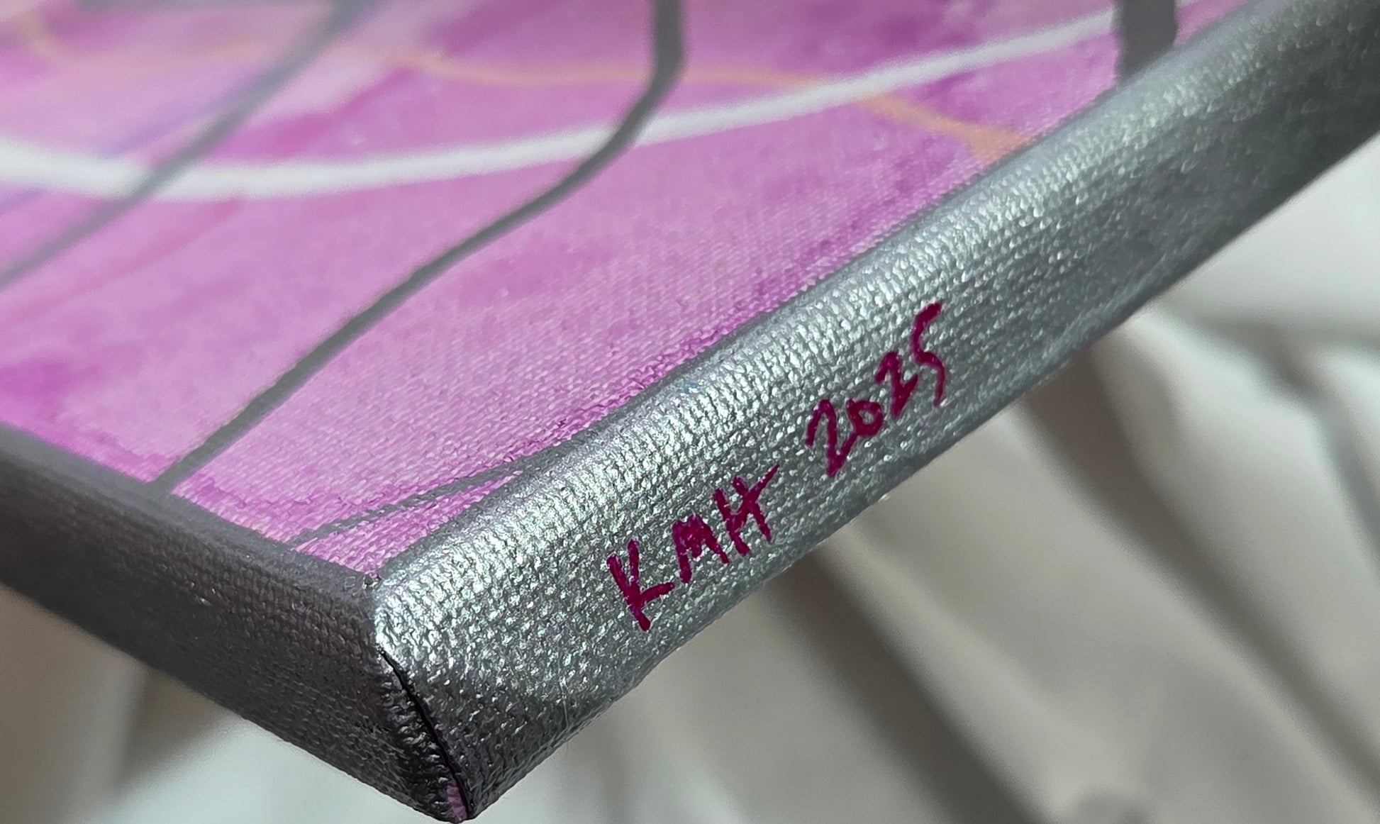 Close-up detail of the silver painted edge of the canvas with the artist's initials and year of creation. The variegated fuchsia and lines is out of focus.