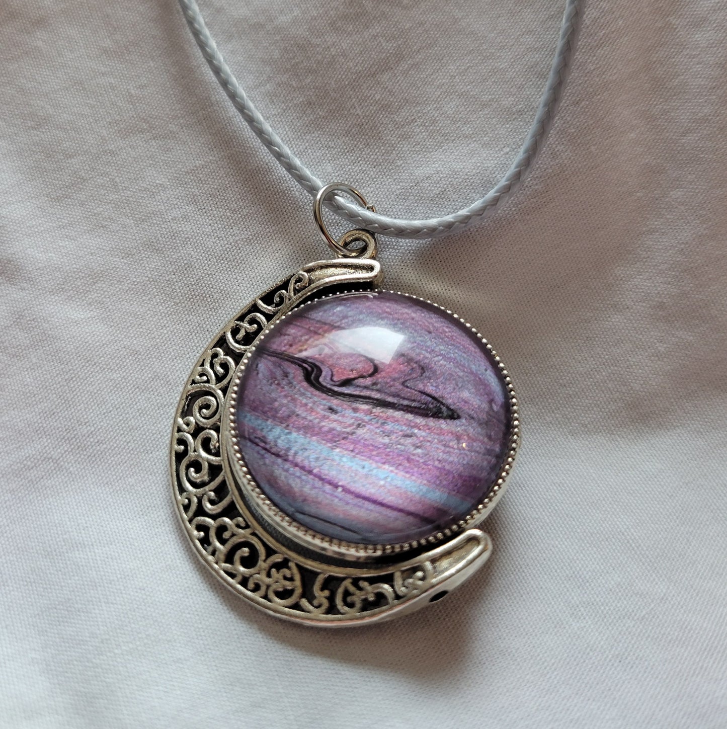 The reverse side of the pendant with more banded striations of blues, pinks, and purples. Some black is twisted through it like a stormy cloud.