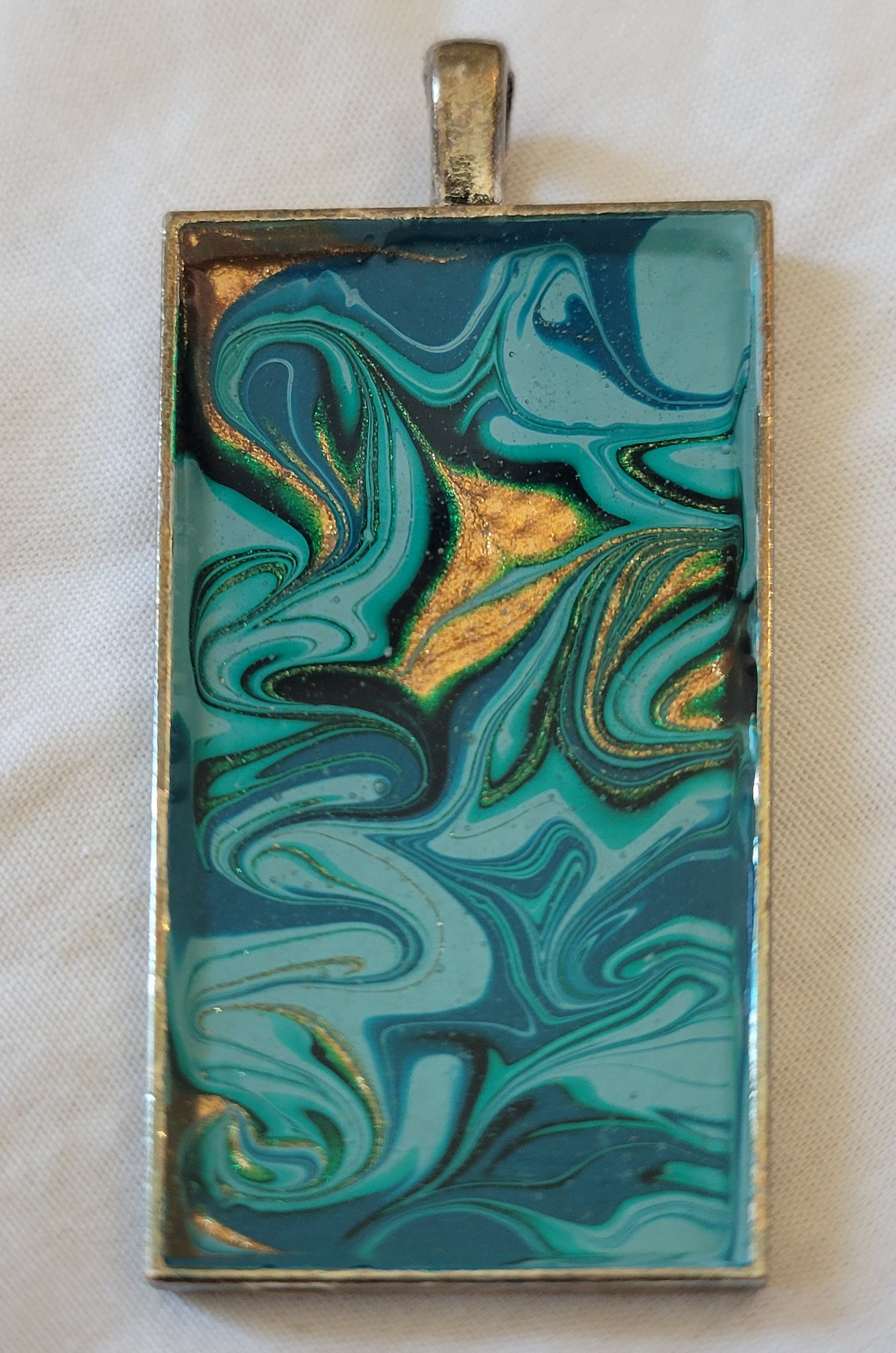 A simple bronze alloy rectangle pendant. Green, turquoise, aqua, and gold are swirled in messy patterns throughout.